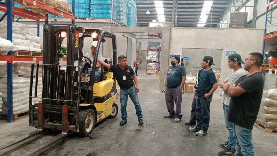 Instructor dando plática de seguridad industrial junto a un montacargas